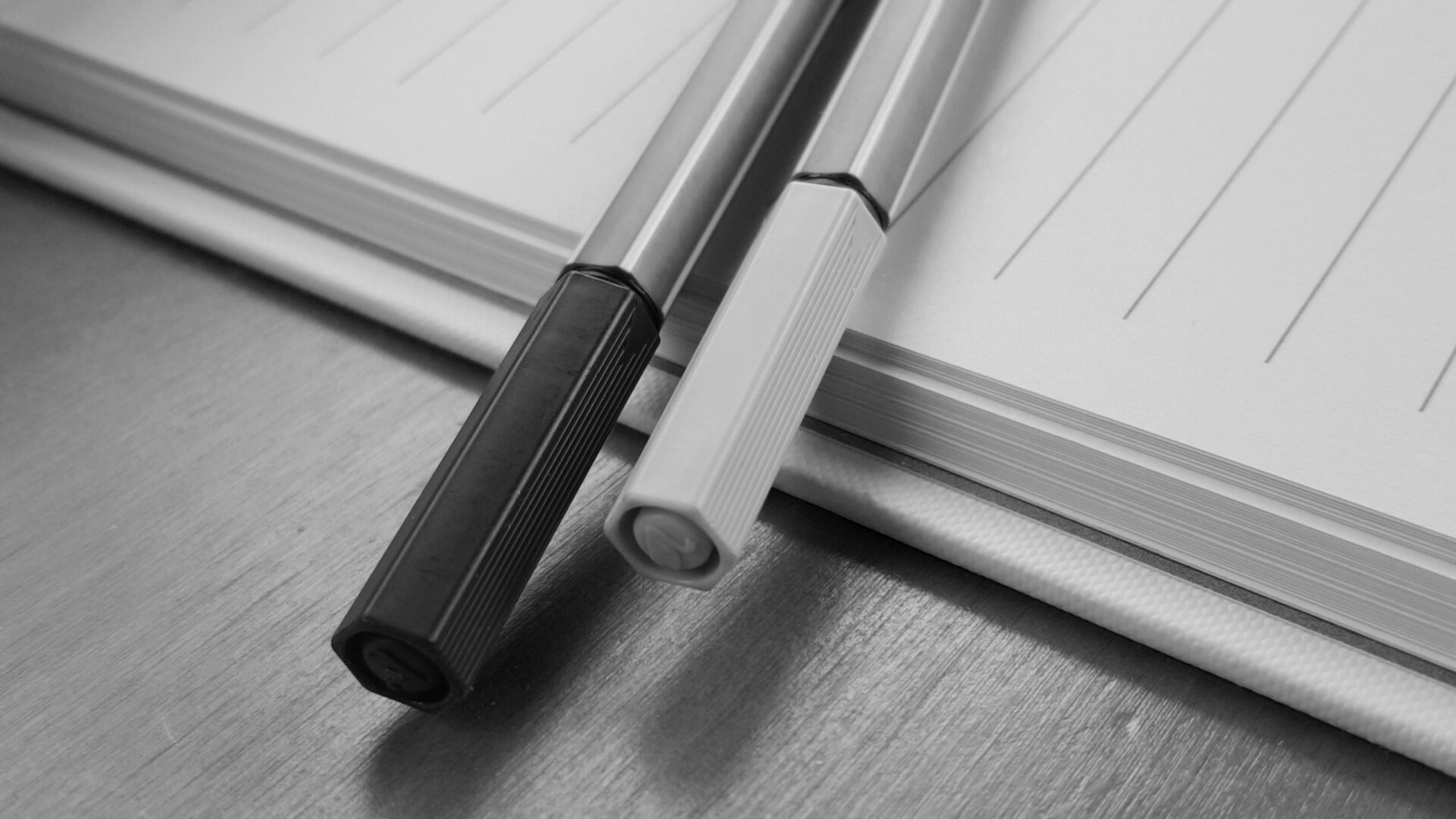 black and white close-up of two pens lying across an open notebook