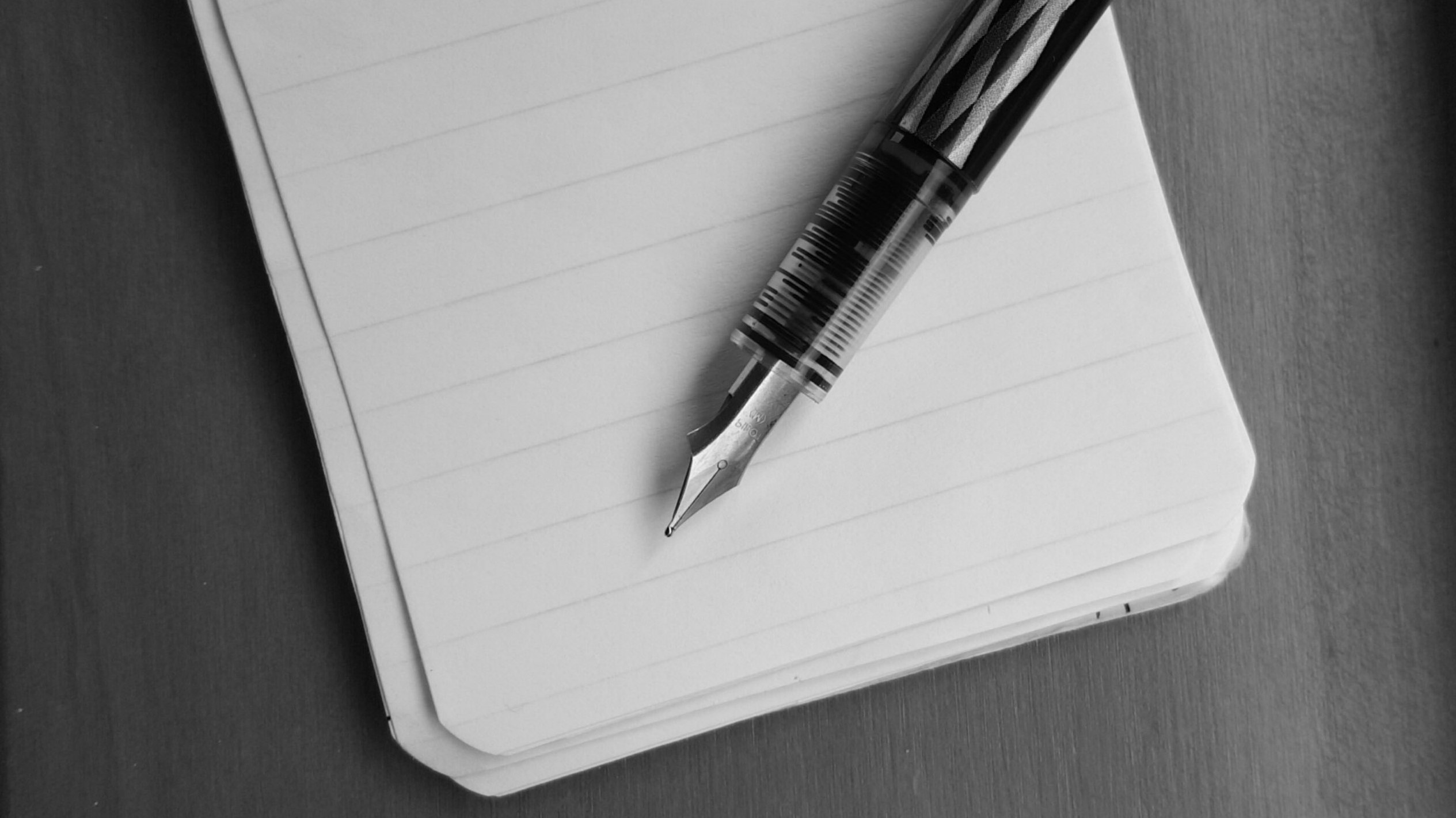black and white picture of an ink pen lying across a small notepad